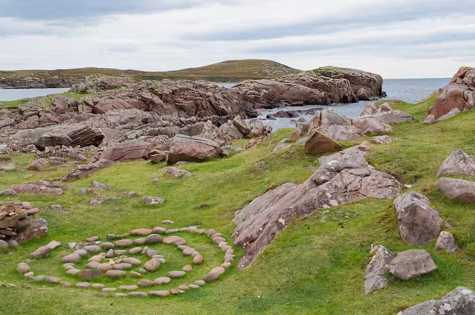 Ein Küstenstreifen auf der Isle of Lewis in Schottland befindet. Im Vordergrund ist ein Steinkreis zu sehen.