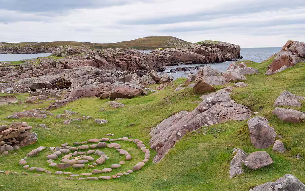 Ein Küstenstreifen auf der Isle of Lewis in Schottland befindet. Im Vordergrund ist ein Steinkreis zu sehen.