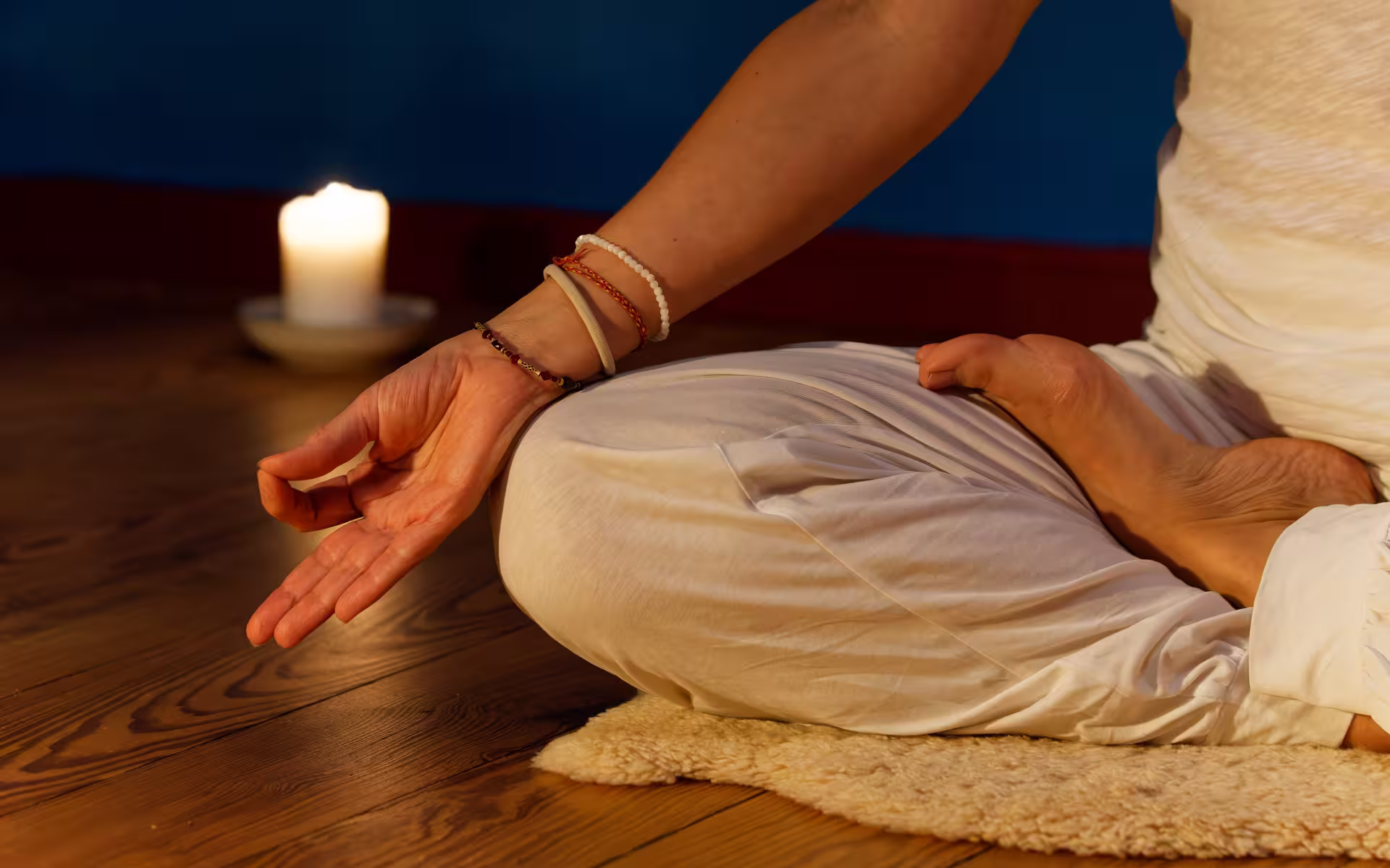 Yoga-Fotografie einer Frau im Yogasitz im Vordergrund. Im Hintergrund sieht man eine brennende Kerze